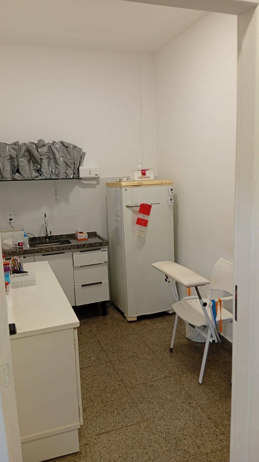 Sala de coleta com bancada, pia e refrigerador para armazenamento de amostras.